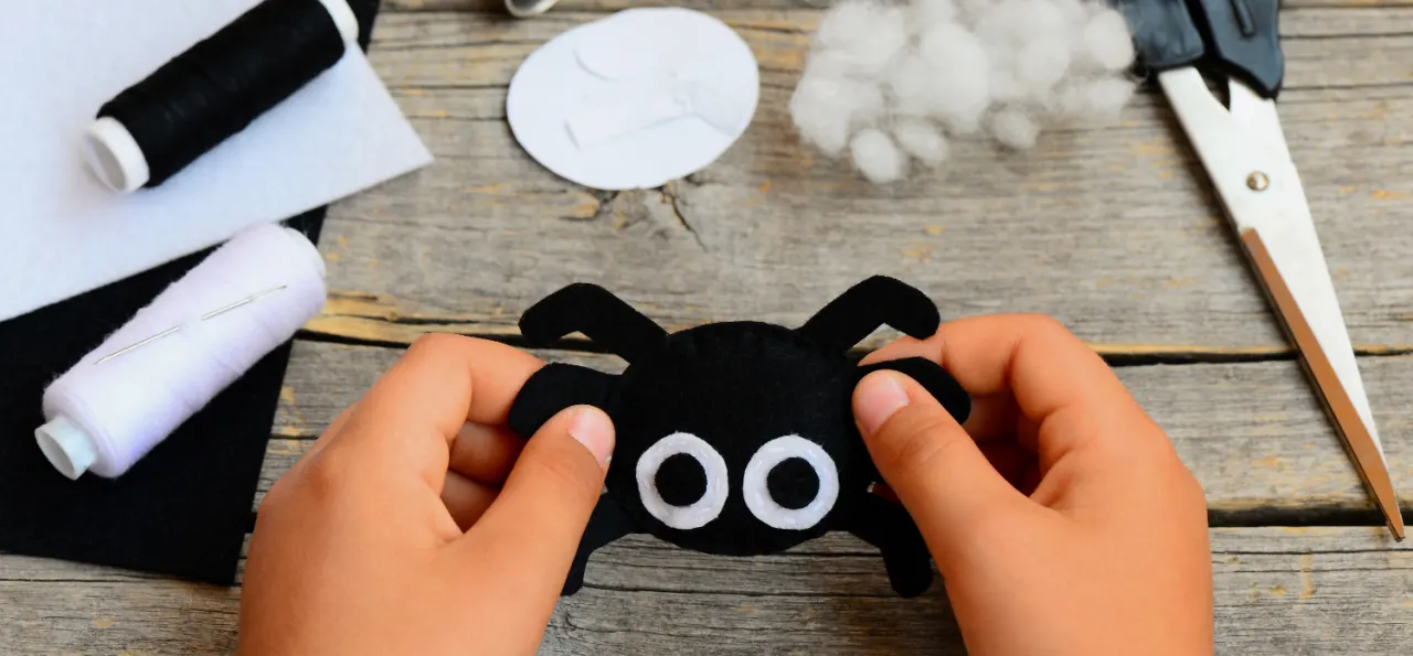 Small child holds a felt spider toy in his hand. Child made a Halloween felt spider crafts. Sewing workshop concept. Teaching a child to sew by hand