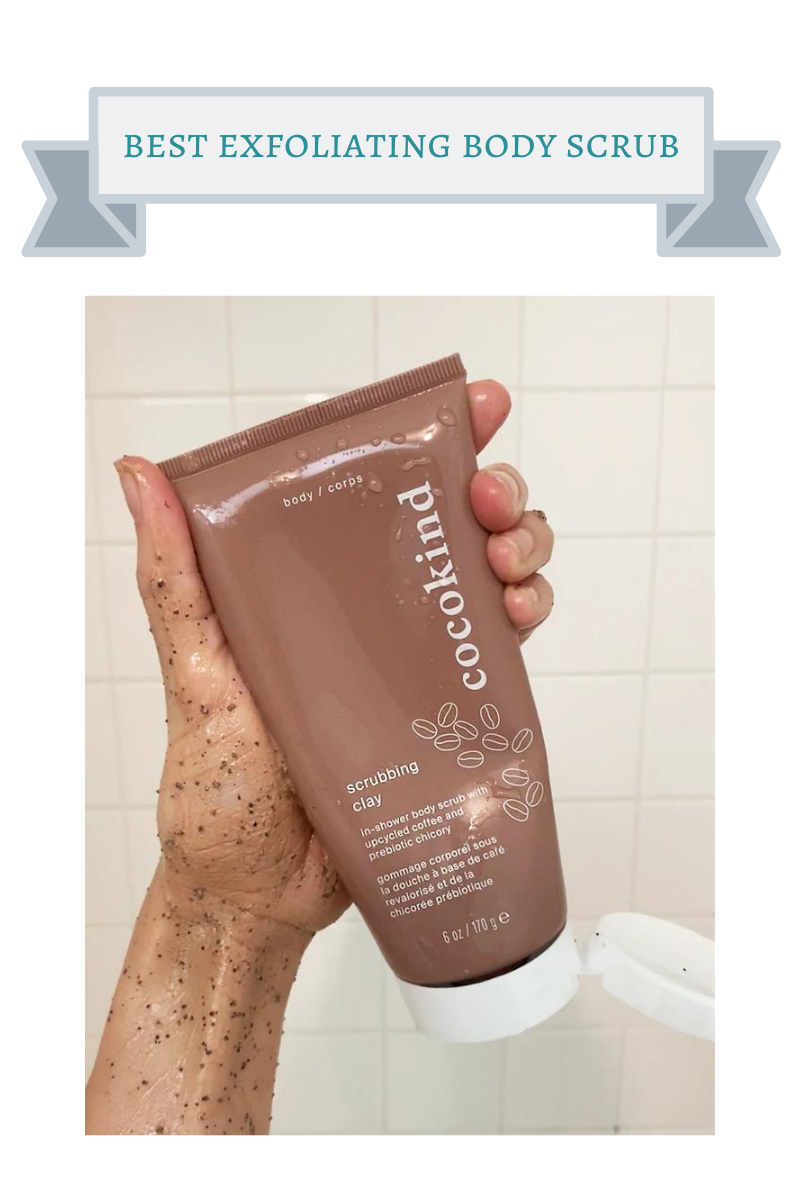 brown tube of cocokind scrubbing clay held by hand in front of white square shower tile