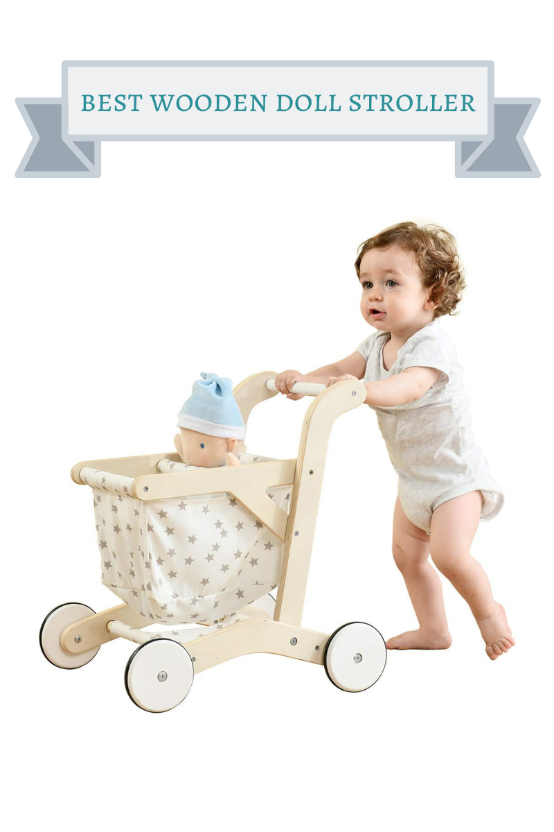 little girl with brown curls pushing a light wood doll stroller with off white basket with silver stars and doll in it with blue hat